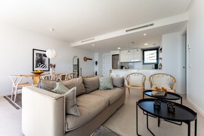 A modern living room with a sofa, chairs, a small table, and a kitchen in the background.