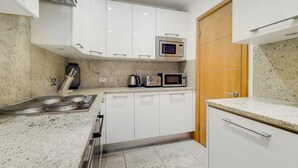 A modern kitchen with white cabinets, a microwave, a kettle, and a stove. - Spacious Knightsbridge Apartment Near Harrods (London)