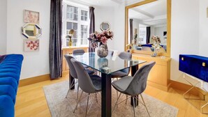 A modern dining area with a glass table, grey chairs, and a vase of flowers. - Spacious Knightsbridge Apartment Near Harrods (London)