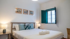 Ein Schlafzimmer mit einem Bett, zwei Nachttischen, einem Fenster mit grünen Rollläden und drei gerahmten Bildern an der Wand.