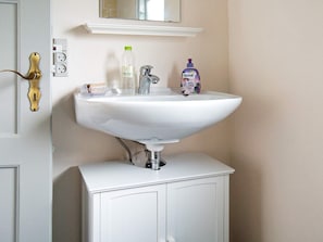 A bathroom with a white sink, a mirror above it, and a door with a brass handle.