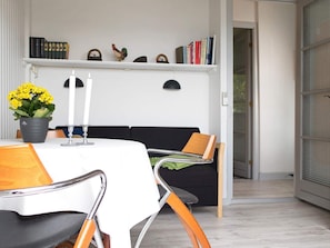 A dining area with a table set for two, a potted plant, and a bookshelf with books and decorative items.