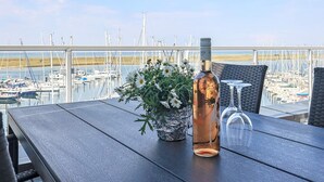 Uma mesa com uma garrafa e um arranjo de flores, com vista para uma marina com barcos.