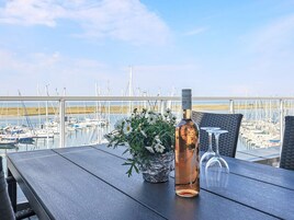 A table with a bottle and a flower arrangement, overlooking a marina with boats.