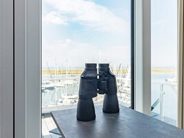 Binoculares sobre una mesa junto a una ventana con vista a un puerto deportivo y barcos.