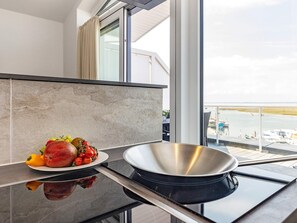 A modern kitchen with a large window, a stainless steel pan, and a plate of fruit.