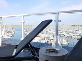 A balcony with a view of a marina, a glass pitcher, and a pair of glasses on a table.
