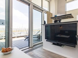 A modern living room with a large flat-screen TV, a sliding glass door leading to an outdoor balcony with a view of boats and a marina.
