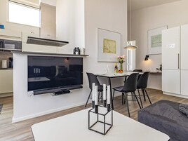 A modern kitchen with a flat-screen TV, dining area with chairs, and a table.