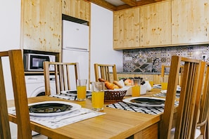 A wooden dining table set with plates, glasses, and a basket of bread.