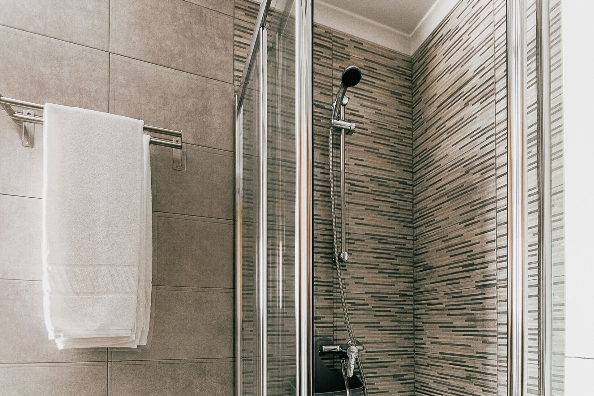 Eine moderne Dusche mit Glastür, Duschbrause und Handtuchhalter mit weißem Handtuch.