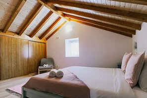 A bedroom with a sloped ceiling, a bed with pillows, a chair, and a small window.
