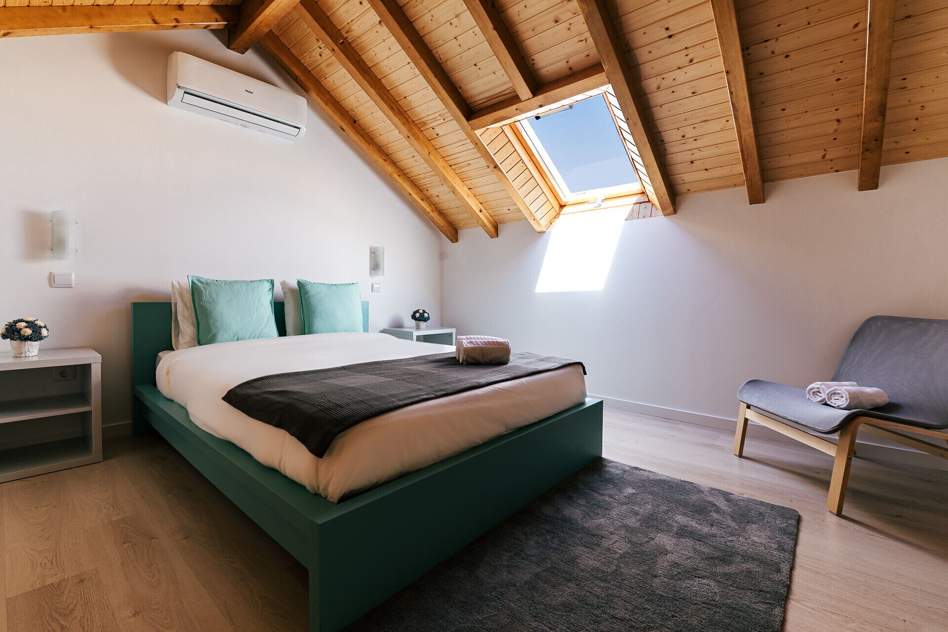 A bedroom with a sloped ceiling, a skylight, a bed, a chair, and a nightstand.