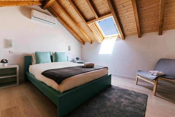A bedroom with a sloped ceiling, a skylight, a bed, a chair, and a nightstand.
