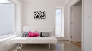 A white sofa with patterned cushions, a wall art piece, and a view through a window. - CASASUPERTUBOS - APART T1 (Atouguia da Baleia)