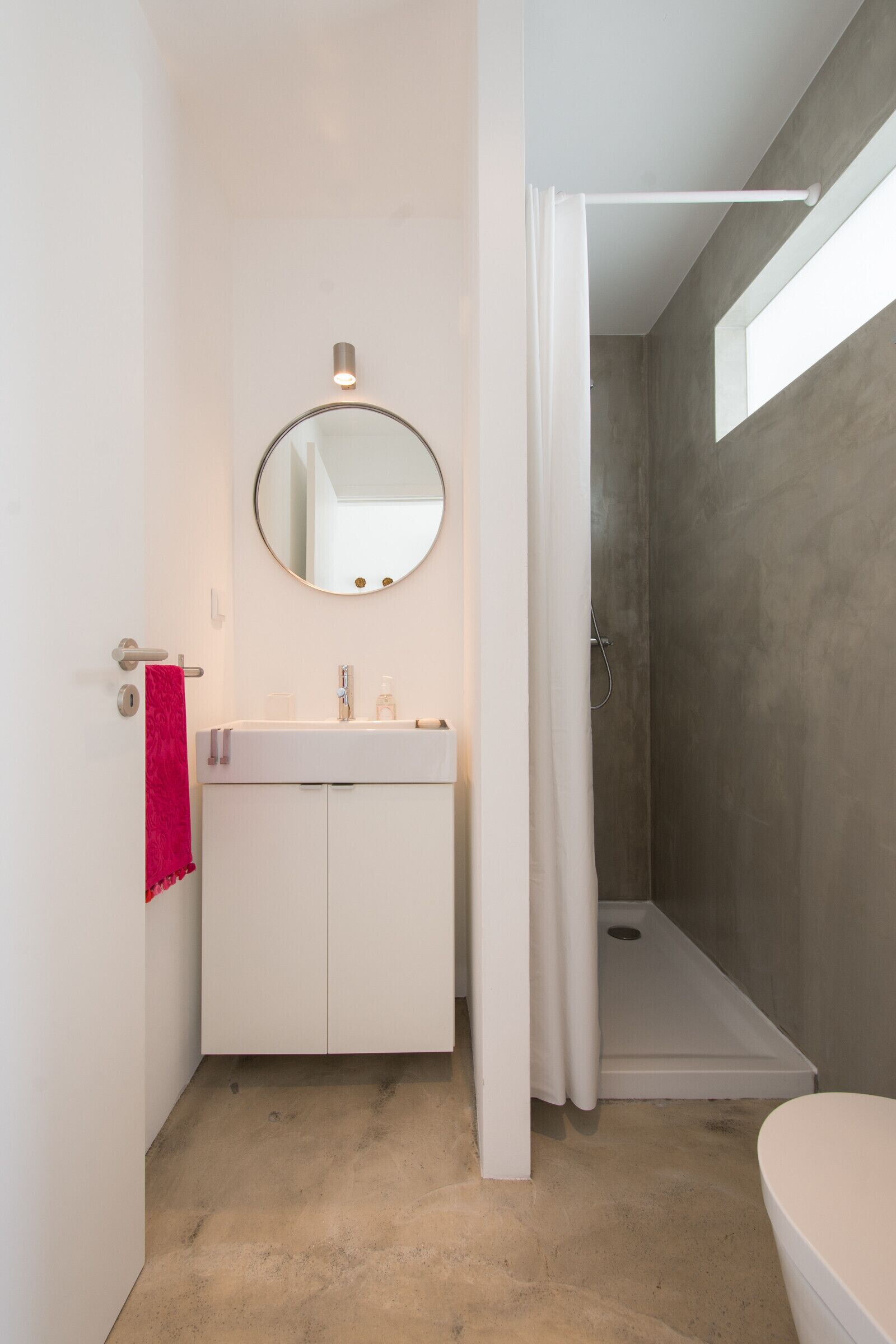 Un baño moderno con un tocador blanco, un espejo redondo y una zona de ducha.