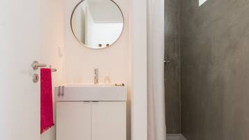 Un baño moderno con un tocador blanco, un espejo redondo y una zona de ducha.