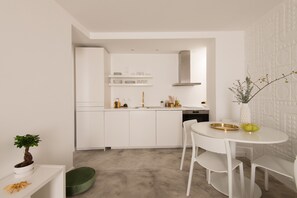 A modern kitchen with white cabinetry, a central island, and a dining area with white chairs and a small table.
