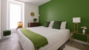 Ein Schlafzimmer mit einem großen Bett, grünen Wänden, einem kleinen Beistelltisch und einem Fenster.