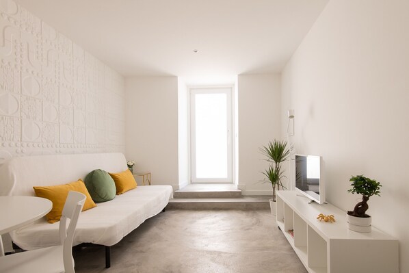 A minimalist living room with a white sofa, a flat-screen TV, and a small potted plant.