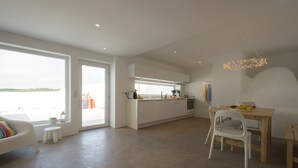 Een moderne keuken met een groot eiland, een eethoek met een houten tafel en stoelen, en uitzicht op het water door grote ramen.