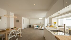 Een moderne keuken met een groot eiland, witte stoelen en een eethoek met een tafel en stoelen.