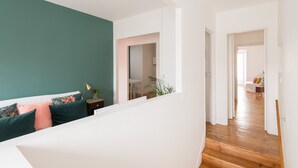 A modern living room with a teal accent wall, a white sofa with colorful pillows, a small side table, and a staircase leading to another room.