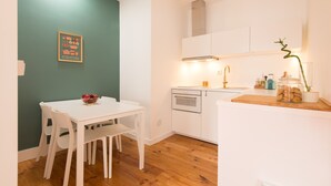 A small, modern kitchen with white cabinetry, a wooden countertop, and a dining table with chairs.