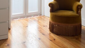 Una habitación con piso de madera, un sillón de color mostaza con detalles de flecos y una puerta blanca con paneles de vidrio.