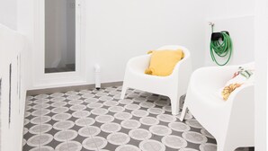 A room with a patterned floor, white walls, a door, and two white chairs with cushions. - CASASUPERTUBOS - APART 14 (Peniche)