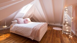 A bedroom with a sloped ceiling, a bed with white bedding, a vanity with lights, and a wooden floor. - CASASUPERTUBOS - APART 14 (Peniche)