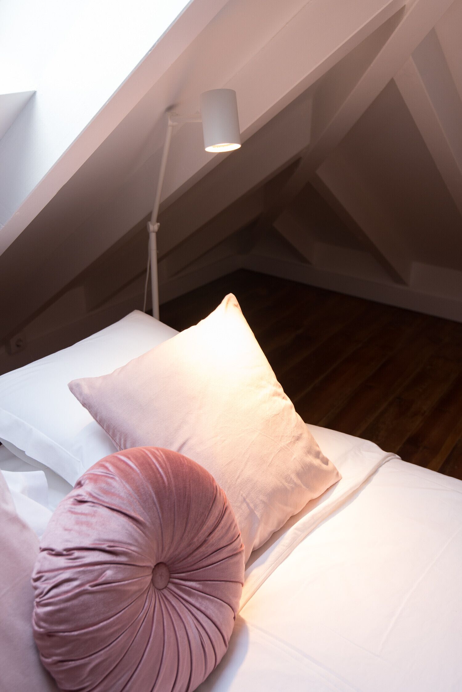 A bedroom with a sloped ceiling, a bed with white and pink bedding, and a floor lamp.