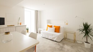 A modern hotel room with a white sofa, a dining table, a TV, and a potted plant. - CASASUPERTUBOS - APART 11 (Peniche)