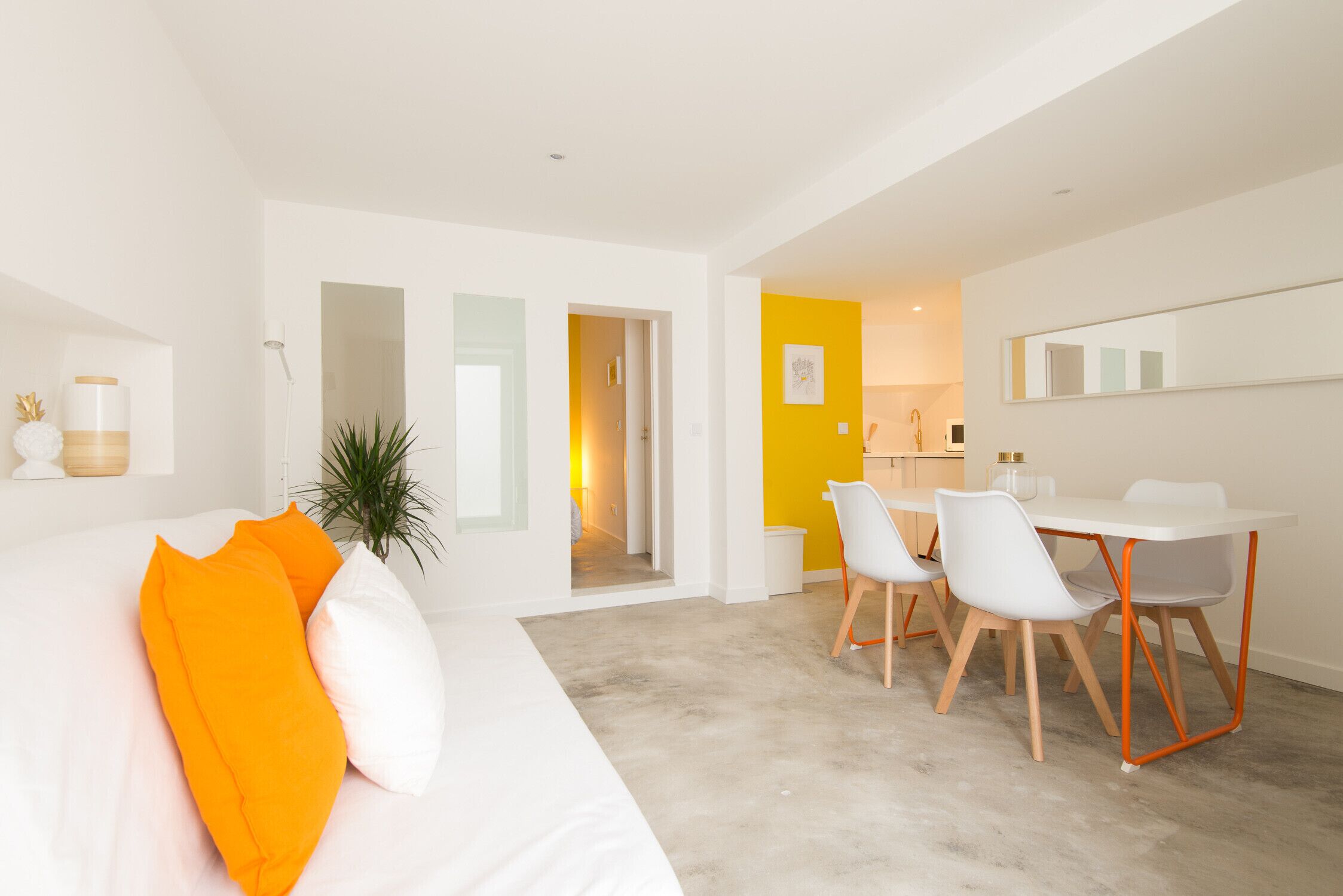 Una habitación de hotel moderna con una cama, un comedor con sillas, una pequeña cocina y un pasillo que conduce a otra habitación.