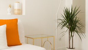 A bedroom with a bed, a bedside table, a lamp, a potted plant, and a wall-mounted shelf with decorative items. - CASASUPERTUBOS - APART 11 (Peniche)