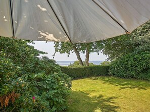 A garden with a lawn, dense foliage, and a view of the sea. - 6 Person Holiday Home in Aakirkeby (Akirkeby)