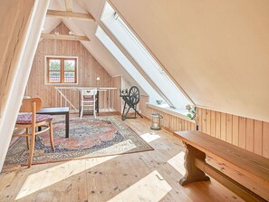 A loft bedroom with a sloped ceiling, wooden walls, a large window, a spinning wheel, a bench, and a table with a chair. - 6 Person Holiday Home in Aakirkeby (Akirkeby)