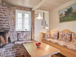 A cozy room with a stone wall, a wooden bench with floral cushions, a wooden table with a red bowl, and a painting on the wall. - 6 Person Holiday Home in Aakirkeby (Akirkeby)