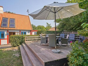 A wooden deck with outdoor furniture, a large umbrella, and a house with a red-tiled roof.