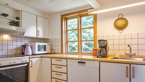 A kitchen with white cabinets, a microwave, a coffee maker, and a window with a view of trees. - 6 Person Holiday Home in Aakirkeby (Akirkeby)