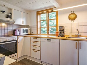 A kitchen with white cabinets, a microwave, a coffee maker, and a window with a view of trees. - 6 Person Holiday Home in Aakirkeby (Akirkeby)