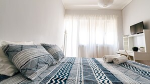 Un dormitorio ordenado con cama, almohadas, televisor y mesita de noche.