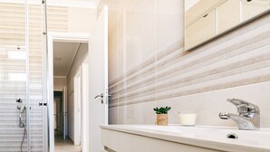 Un baño con cabina de ducha de vidrio, un lavamanos con espejo y una planta en el mostrador.