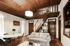 A cozy living room with a wooden staircase, a white sofa, a dining table, and a hanging light fixture. - Country Village Senses - Casinha (Reguengo Grande)