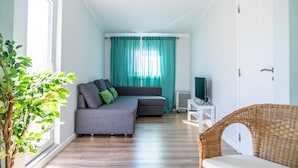 Un salon moderne avec un canapé gris, des rideaux turquoise, un meuble TV blanc et un fauteuil en osier.