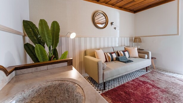 Un salon avec un canapé beige, un tapis rouge, une table basse en marbre, une plante et un plafond en bois.