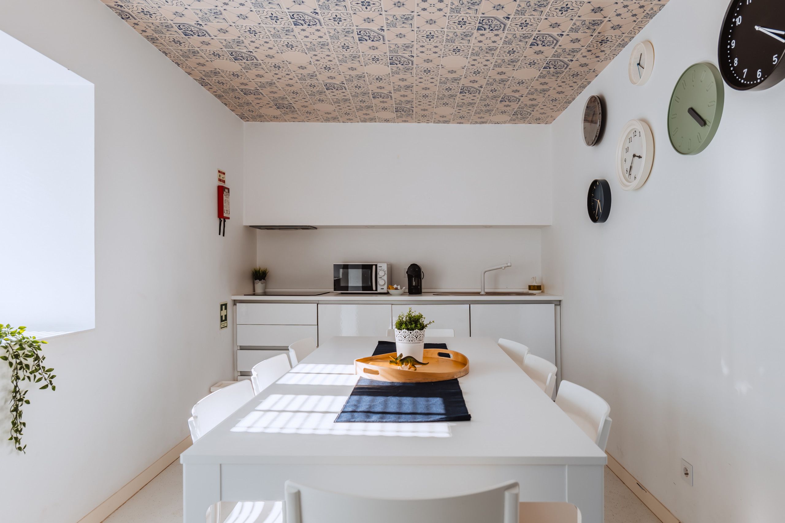 A modern kitchen with white cabinets, a microwave, and a sink. There is a dining table with a tray and a plant.
