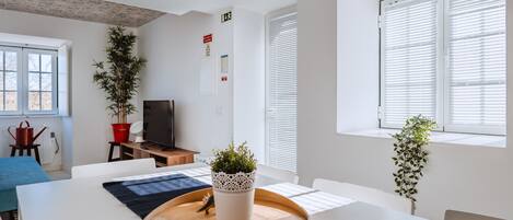 A modern room with a large table, chairs, a television, and potted plants.