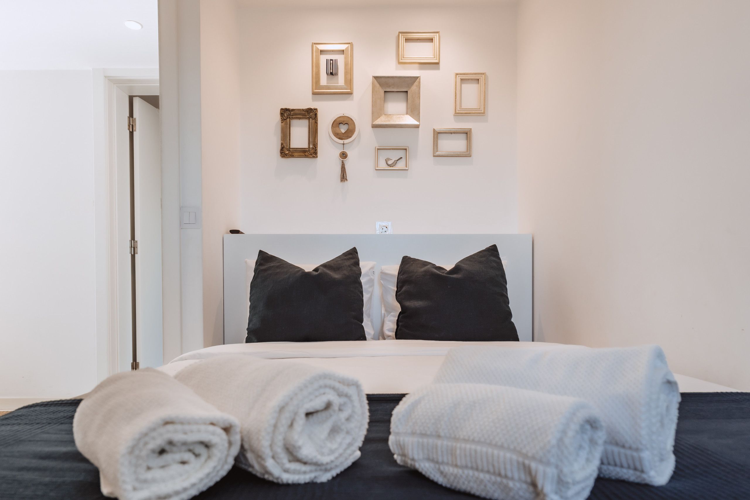 Un lit bien fait, avec des serviettes pliées, une tête de lit et un mur orné de tableaux.