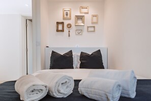 A neatly made bed with rolled towels, a headboard, and a wall with framed pictures. - Encosta d'Óbidos T3 (Óbidos)